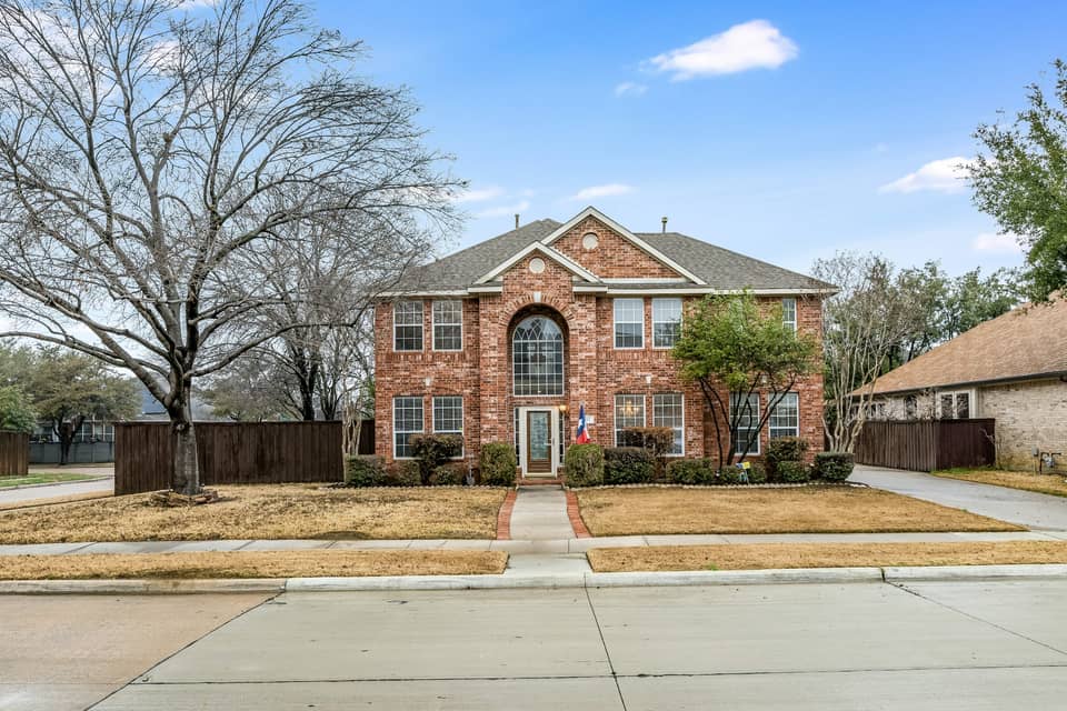 A two-story red brick house on a North Texas suburban street